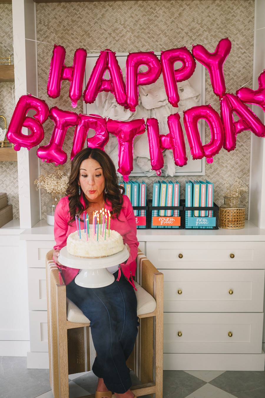 Jamie blowing out birthday candles in front of a giant HAPPY BIRTHDAY balloon banner